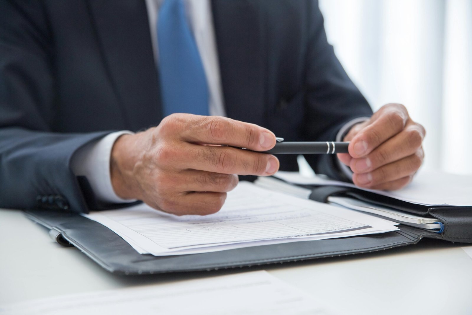 Businessman in suit holding pen, ready to sign documents. Close-up detail shot.
