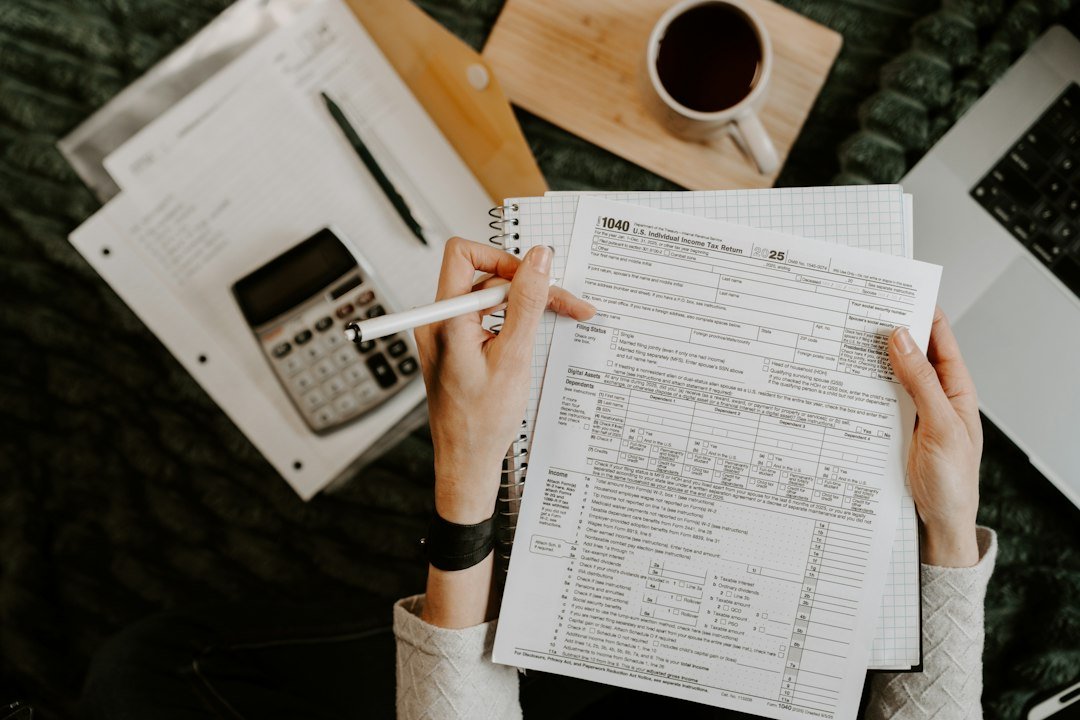 Person reviewing documents with a calculator and a laptop on a desk
