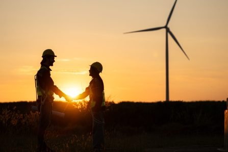 Silhouette of engineer and worker shaking hands on wind turbine background